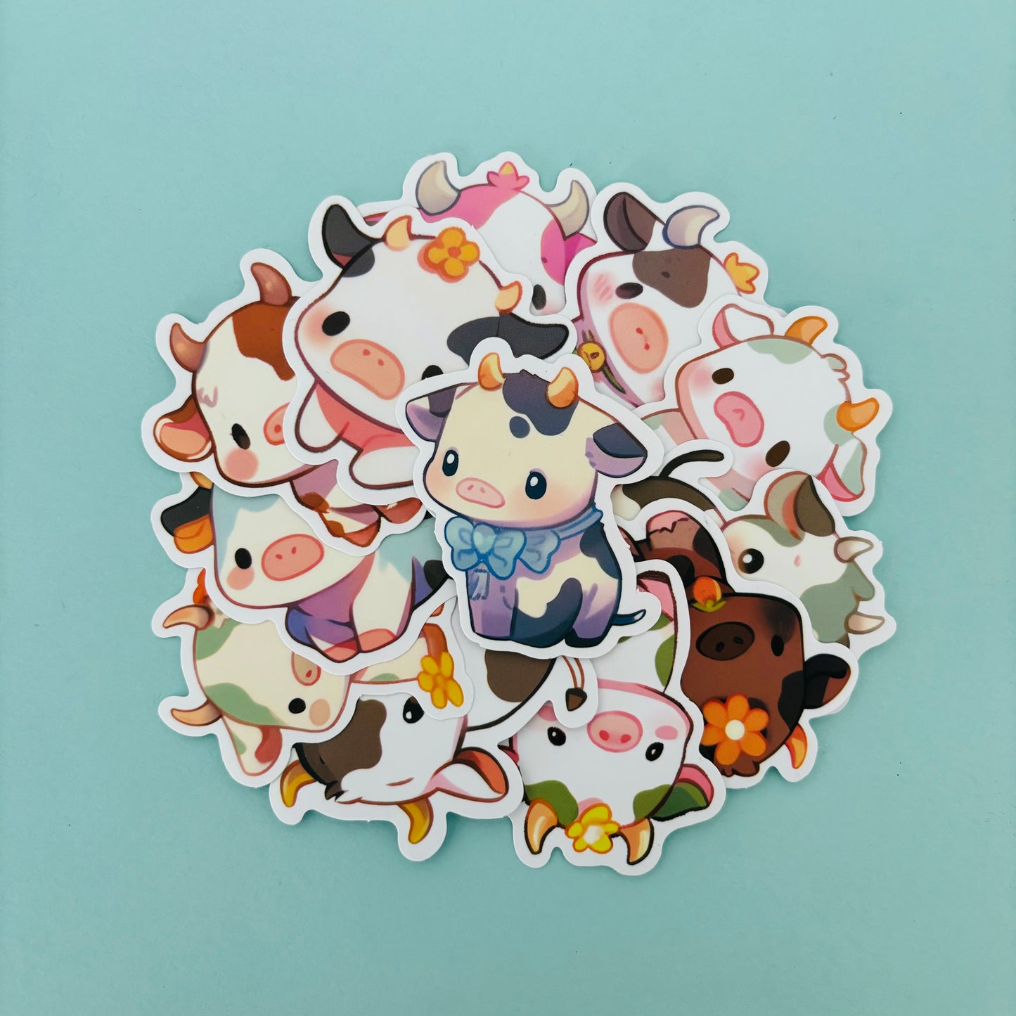 Pile of 15 colorful, kawaii-style cow stickers with different designs and expressions, displayed on a pastel aqua background.