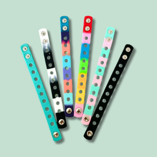 Set of colourful silicone wristbands with circular holes, designed to hold and display shoe charms. Laid out in a fan shape on a mint green background.