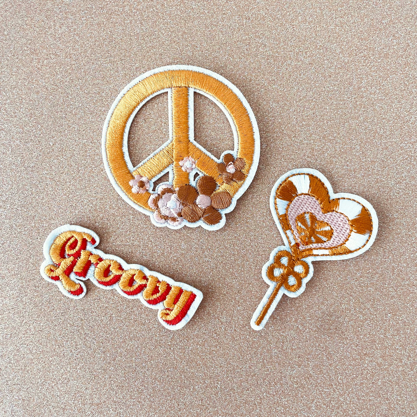 A collection of three clothing patches with peace, love, and groovy designs embroidered in the 1960s style.