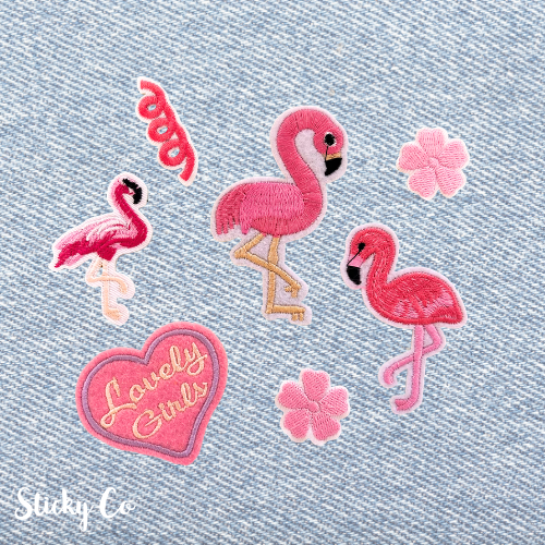 Set of pink flamingo and heart-shaped 'Lovely Girls' patches on a denim background.