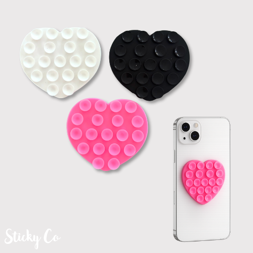 Heart-shaped pop-it fidget toys in white, black, and pink on a white background with a phone case featuring a pink heart-shaped pop-it.